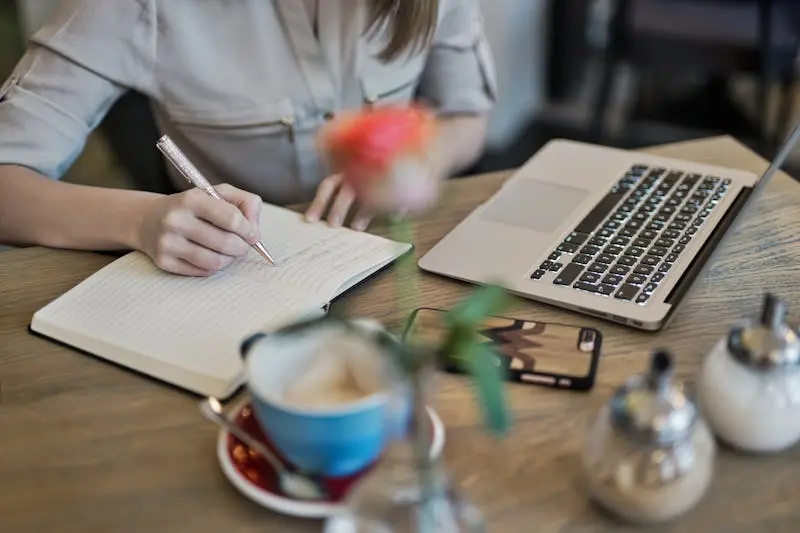 Women taking notes while working on a laptop having Coffee and phone on the table