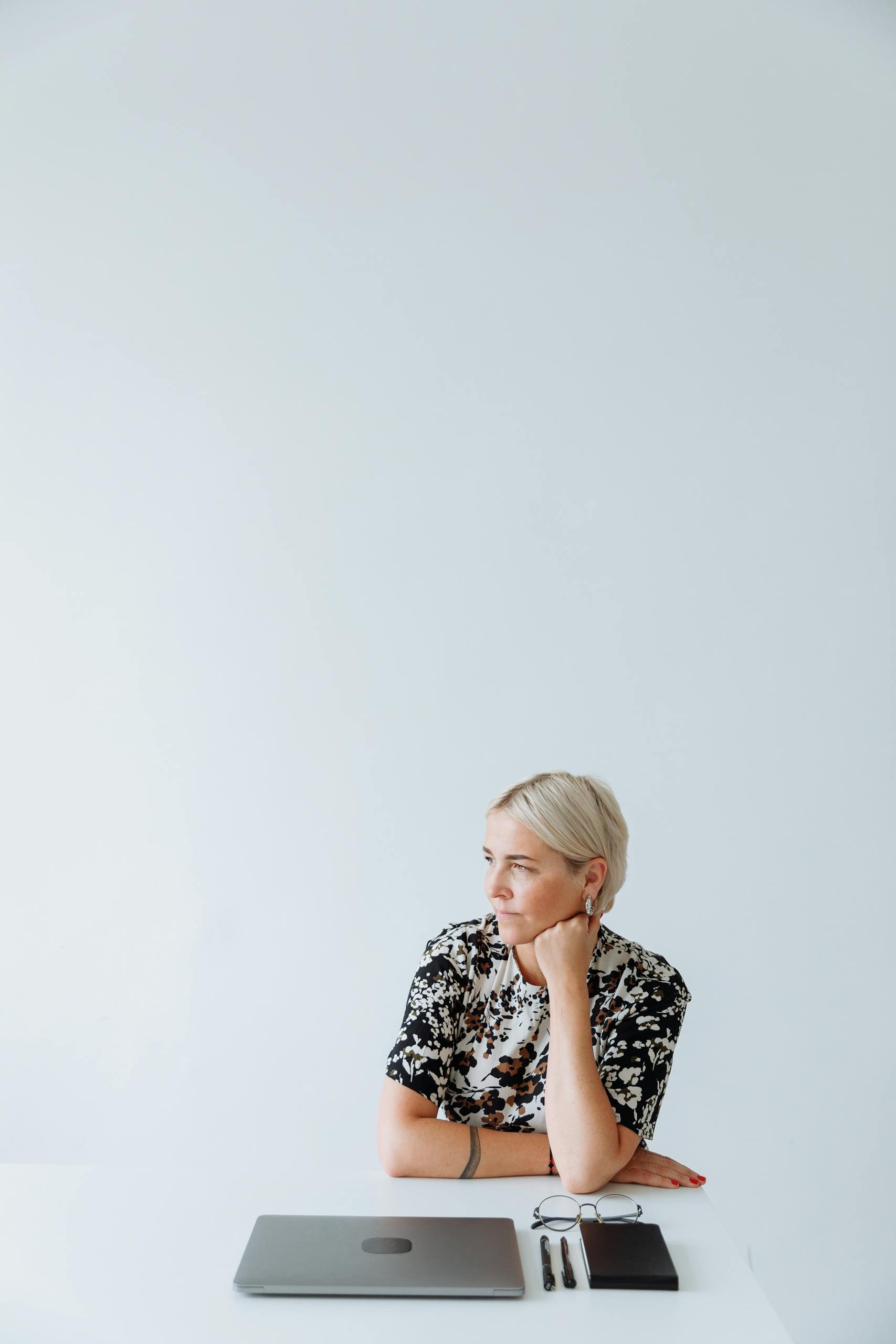 A Woman in Printed Shirt Thinking while Sitting Near the Table with Laptop