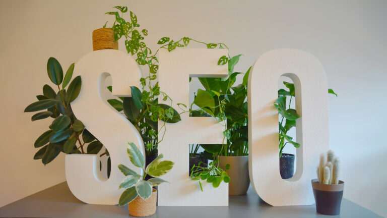 Vibrant and nature-inspired office setting at an SEO agency, featuring large 'SEO' letters prominently displayed on a modern desk. The letters are adorned with an abundance of lush green plants, creating a refreshing and natural atmosphere. The combination of digital focus and greenery brings a unique balance of productivity and tranquility to the workspace.