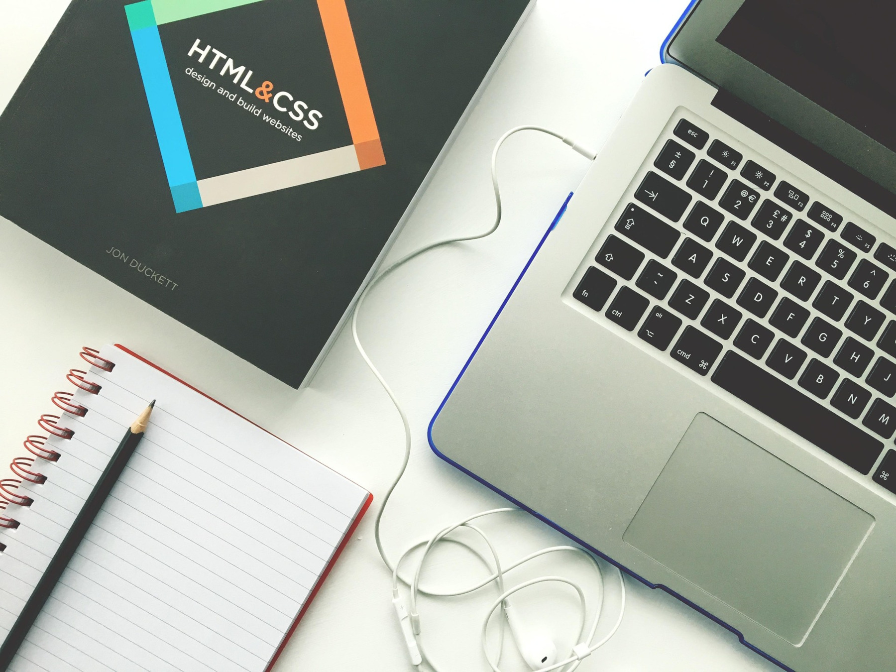 HTML and CSS web development book beside a laptop and notebook on a desk.