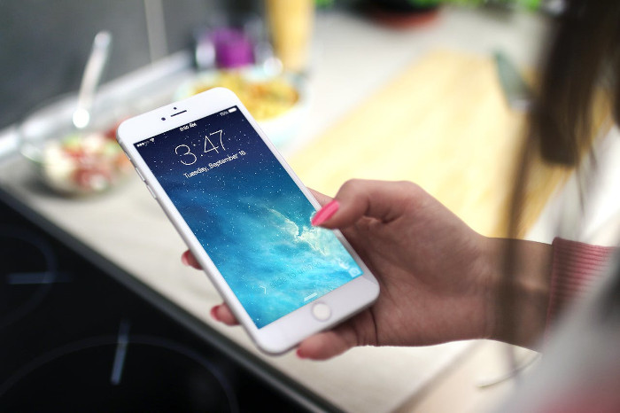 Close-up shot of a person holding a smartphone in a kitchen setting, displaying the lock screen.